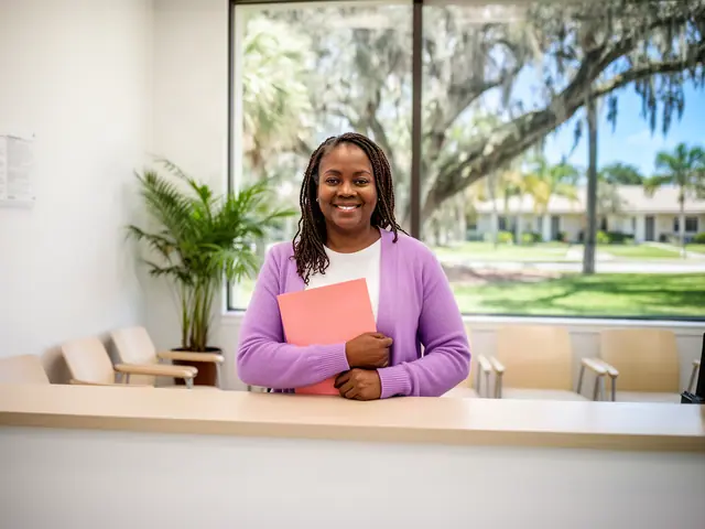 A clinic office manager holding a folder behind a reception counter.